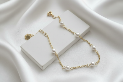 Gold bracelet with pearls on a white stand against a white background