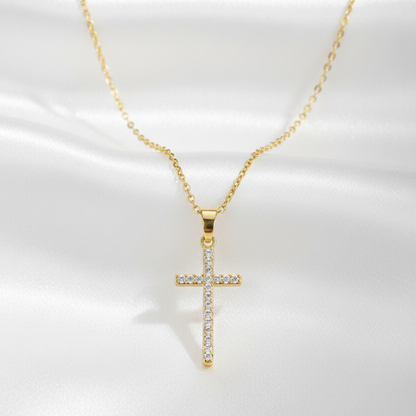A gold cross pendant necklace adorned with small clear stones, displayed on a white satin fabric background.