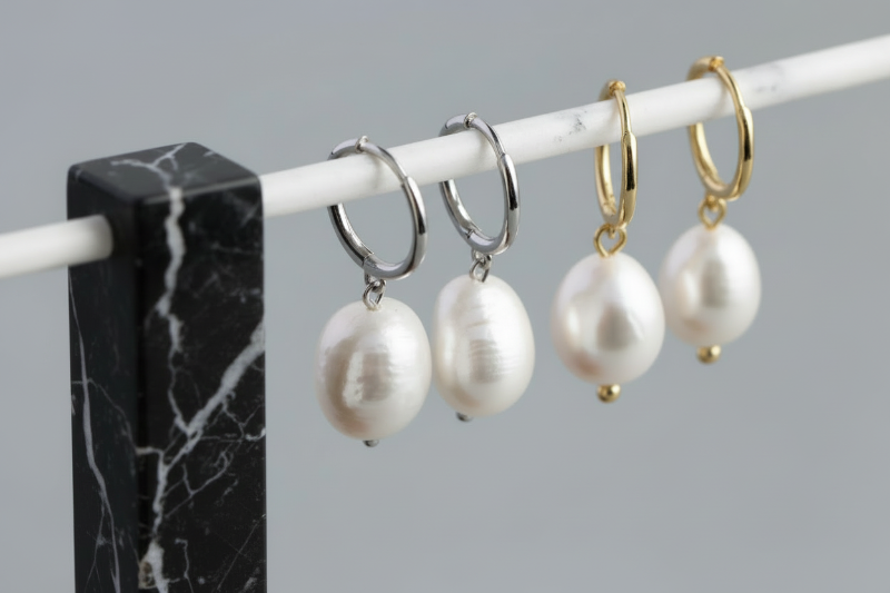 Three pairs of pearl earrings on a marble stand against a grey background