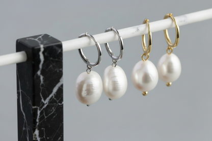 Three pairs of pearl earrings on a marble stand against a grey background