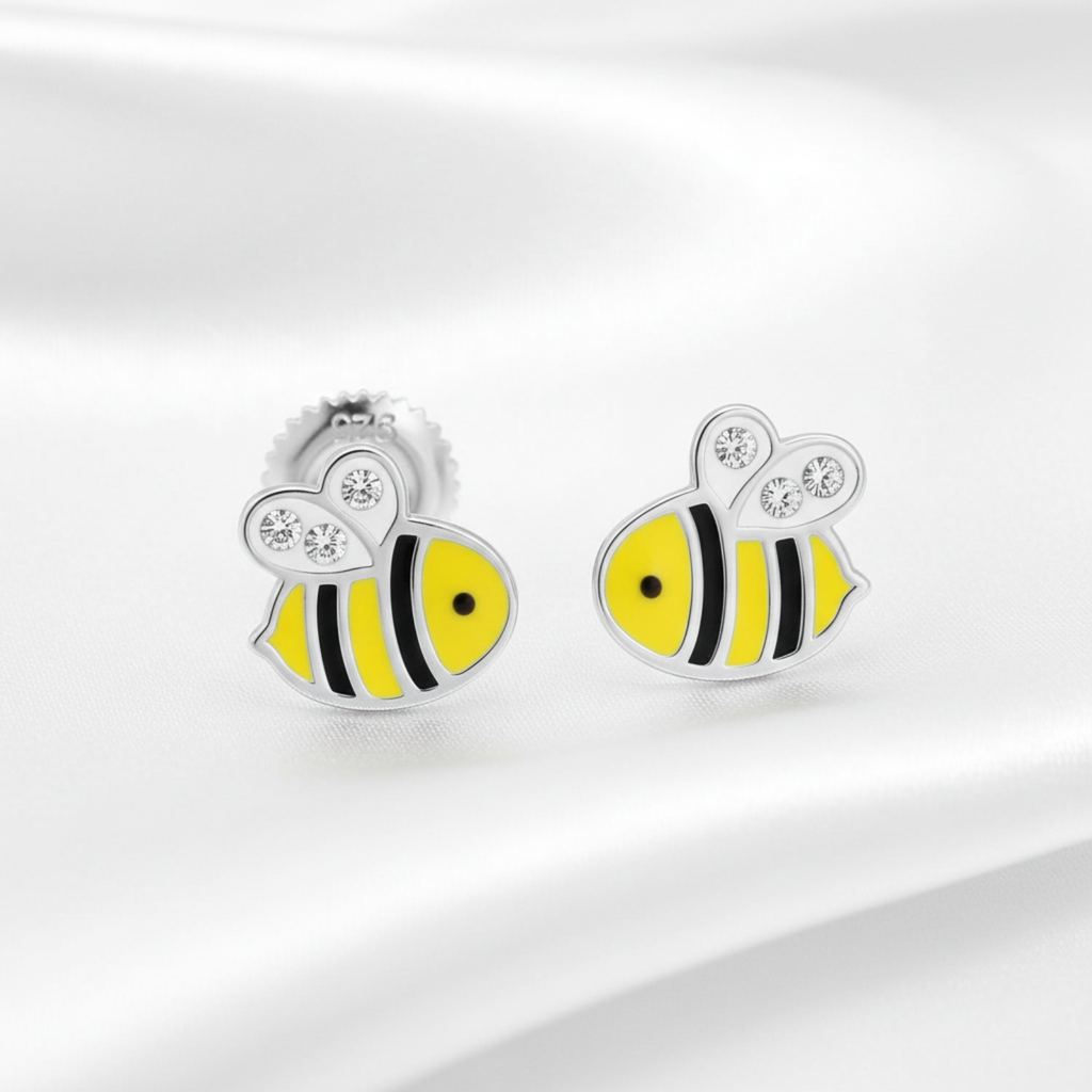 A pair of silver stud earrings shaped like bumblebees, featuring bright yellow enamel bodies with black stripes, clear crystal wings, and silver posts, displayed on a soft white satin fabric.