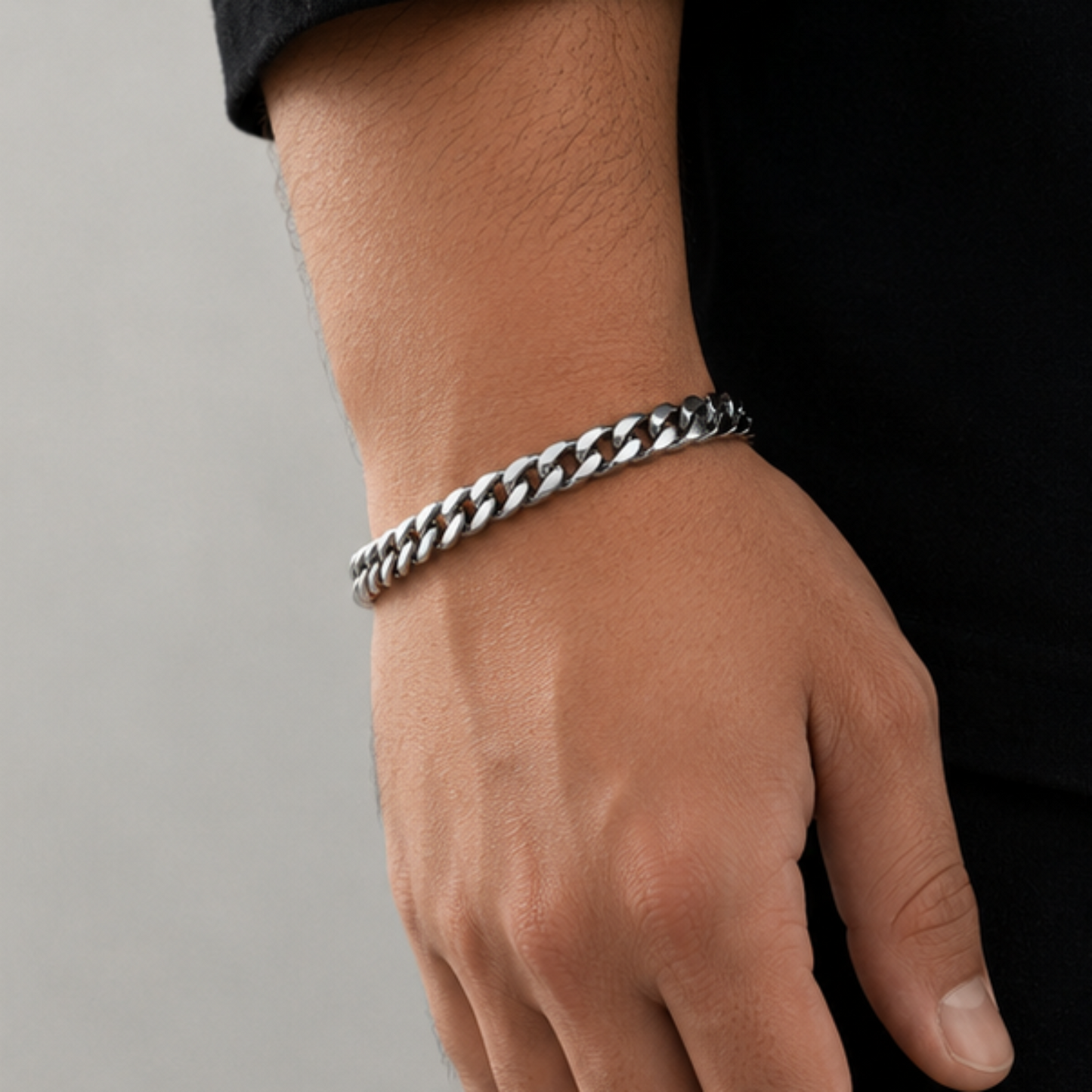 A close-up of a person's wrist and hand wearing a thick silver-toned curb chain bracelet against a dark shirt and light gray background.